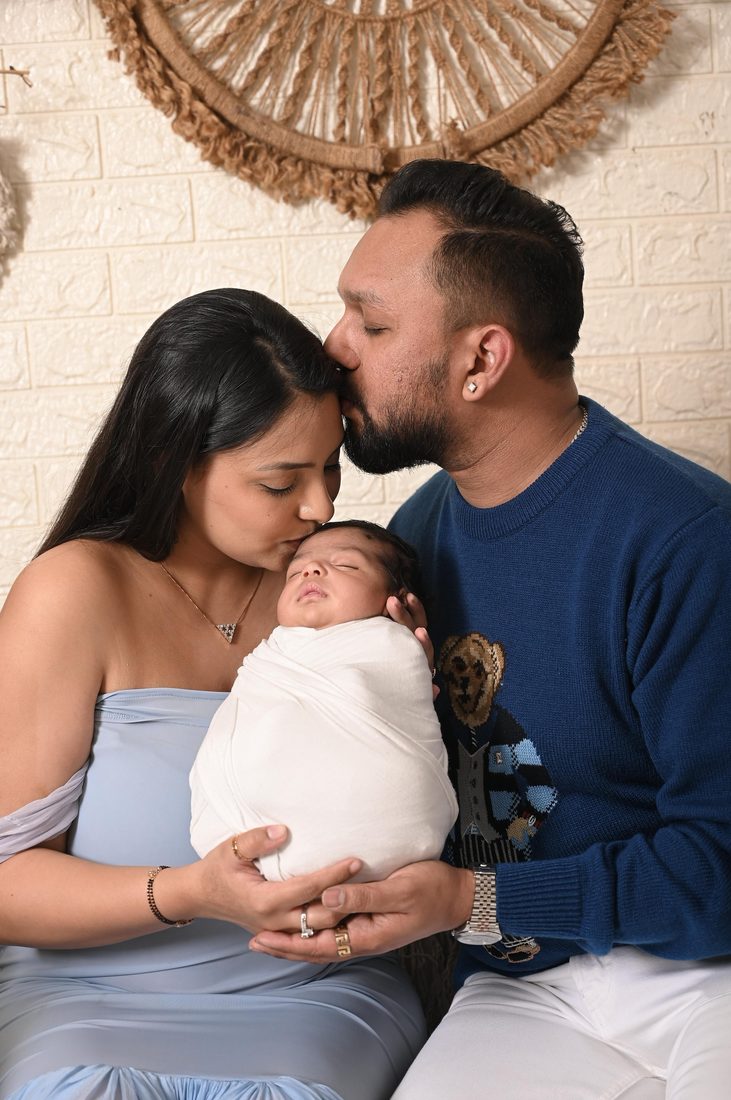 Mum and dad kissing baby Rivaay, swaddled, at home