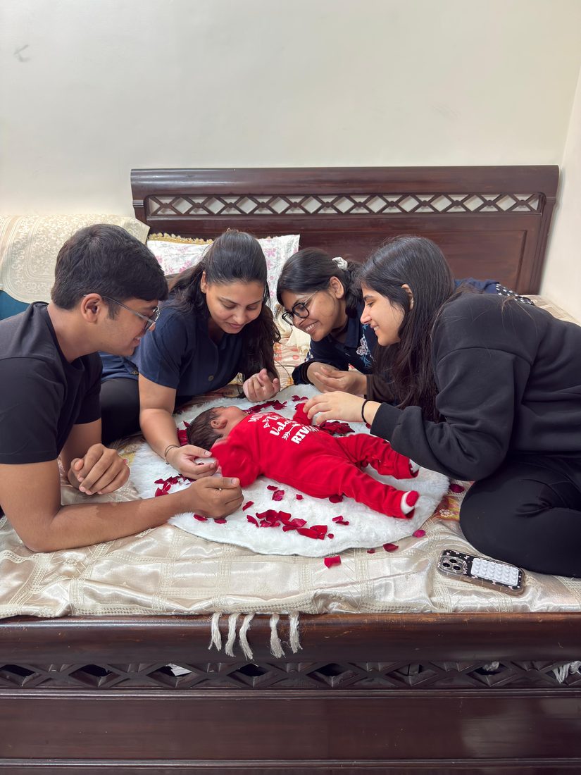 Rivaay in a red outfit surrounded by rose petals, family around him